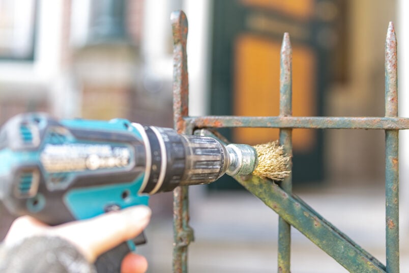 cleaning a rusty metal gate with a drill and wire brush